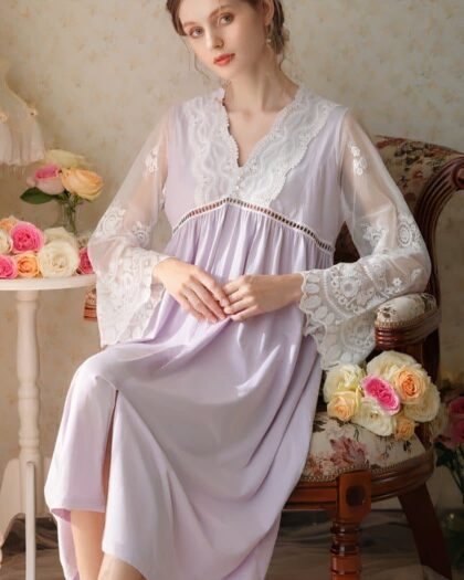 Femme assise sur une chaise portant une nuisette longue violette. Derrière se trouve des fleurs et des coussins