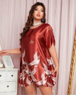 Nuisette grande taille de couleur bronze avec des motifs floraux, portée par une femme debout devant une commode blanche et un rideau rose