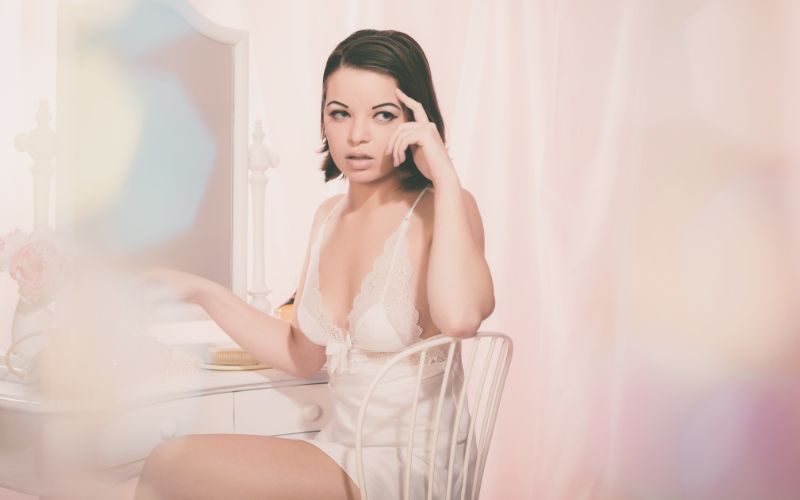 femme brune dans une nuisette et devant une coiffeuse. Dans un ton rose poudré