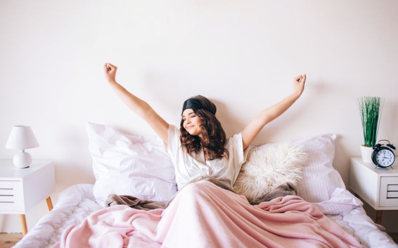 femme dans son lit avec un masque de nuit qui s'étire