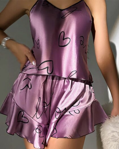 Pyjama Femme Été Satiné Deux Pièces avec Short, de couleur violet avec des motifs de coeurs noirs, porté par une femme.