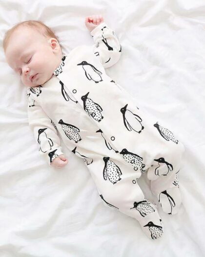 Un bébé endormi portant une combinaison pyjama avec motifs pingouins
