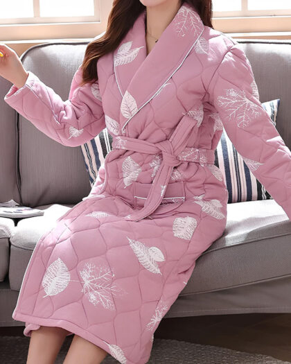 Femme portant une robe de chambre matelassée rose à motifs feuillus, assise sur canapé gris
