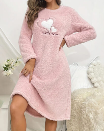 Femme vêtue d'une chemise de nuit hiver rose douce et confortable portant une broderie en forme de cœur au niveau de la poitrine.