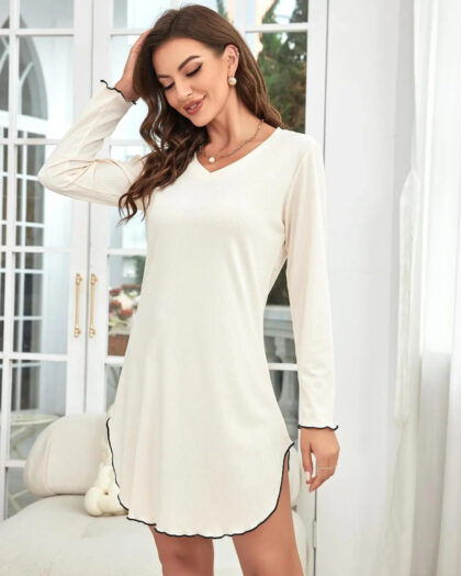 Femme vêtue d'une chemise de nuit d'hiver beige à manche longue laissant apparaitre ces jambes. Elle se tient debout dans son salon